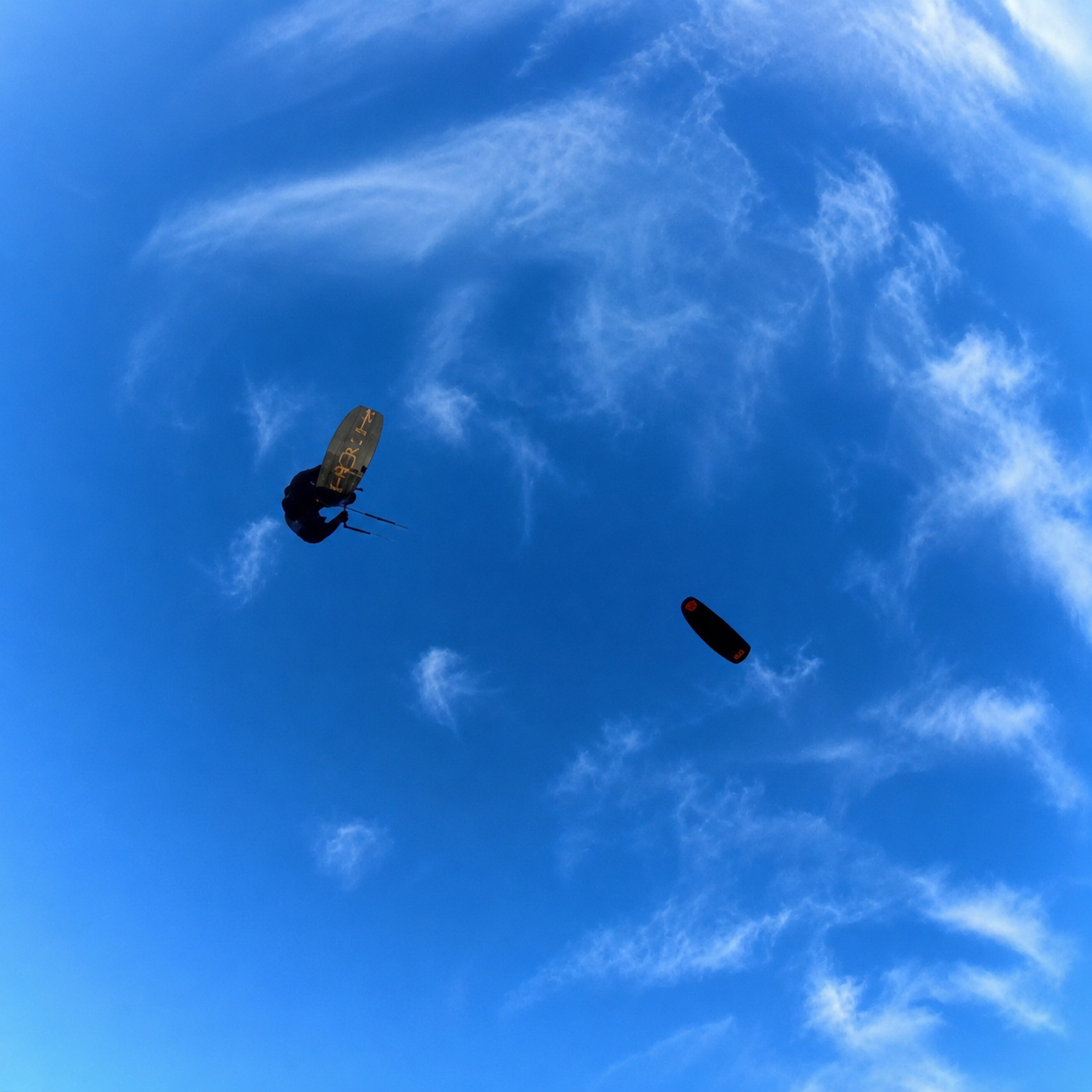 Big-air kitesurfer high against a blue sky
